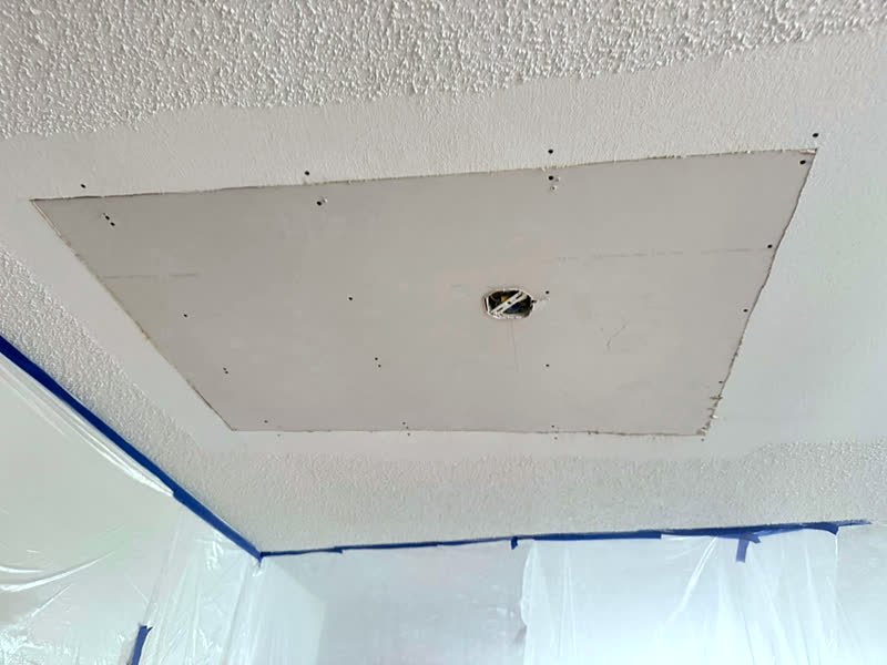 New drywall patch installed in a textured ceiling after water damage